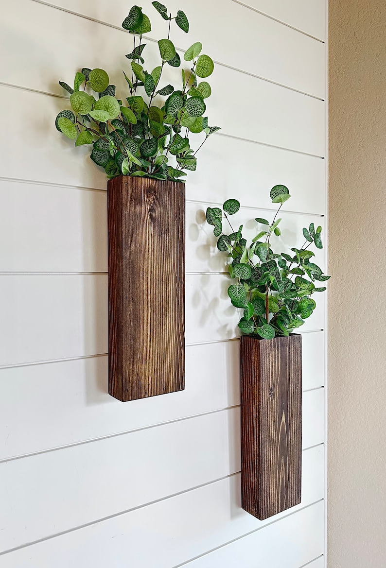 Two handmade rustic wooden wall sconces with a dark, rich wood finish. Wood color is customizable. Each planter holds a vibrant faux eucalyptus plant. Minimalist yet elegant design making this piece perfect for a rustic, farmhouse or bohemian style