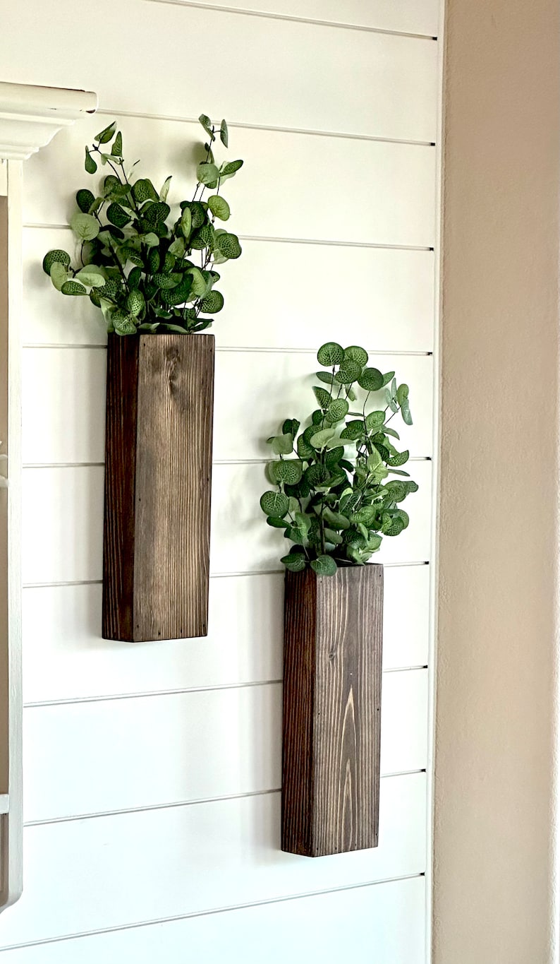 Two handmade rustic wooden wall sconces with a dark, rich wood finish. Wood color is customizable. Each planter holds a vibrant faux eucalyptus plant. Minimalist yet elegant design making this piece perfect for a rustic, farmhouse or bohemian style