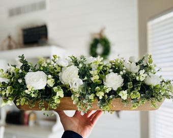 May include: A wooden trough filled with a floral arrangement of white flowers and green foliage. The arrangement is perfect for a centerpiece or home decor.