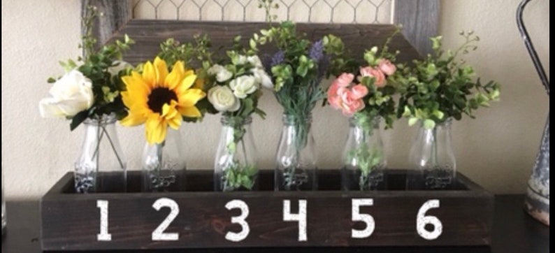 May include: A wooden box with six glass milk bottles, each holding a different type of flower arrangement. The bottles are numbered 1 through 6 on the front of the box.