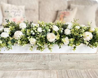 Può includere: Un vassoio di legno bianco pieno di un arrangiamento floreale di rose bianche e fogliame verde.