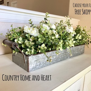 May include: A galvanized metal planter with a rustic handle filled with white flowers and green foliage. The planter is sitting on a white surface with the text "COUNTRY HOME AND HEART" below it. The text "CHOOSE YOUR FLOWERS!! FREE SHIPPING!!" is visible in the upper right corner of the image.