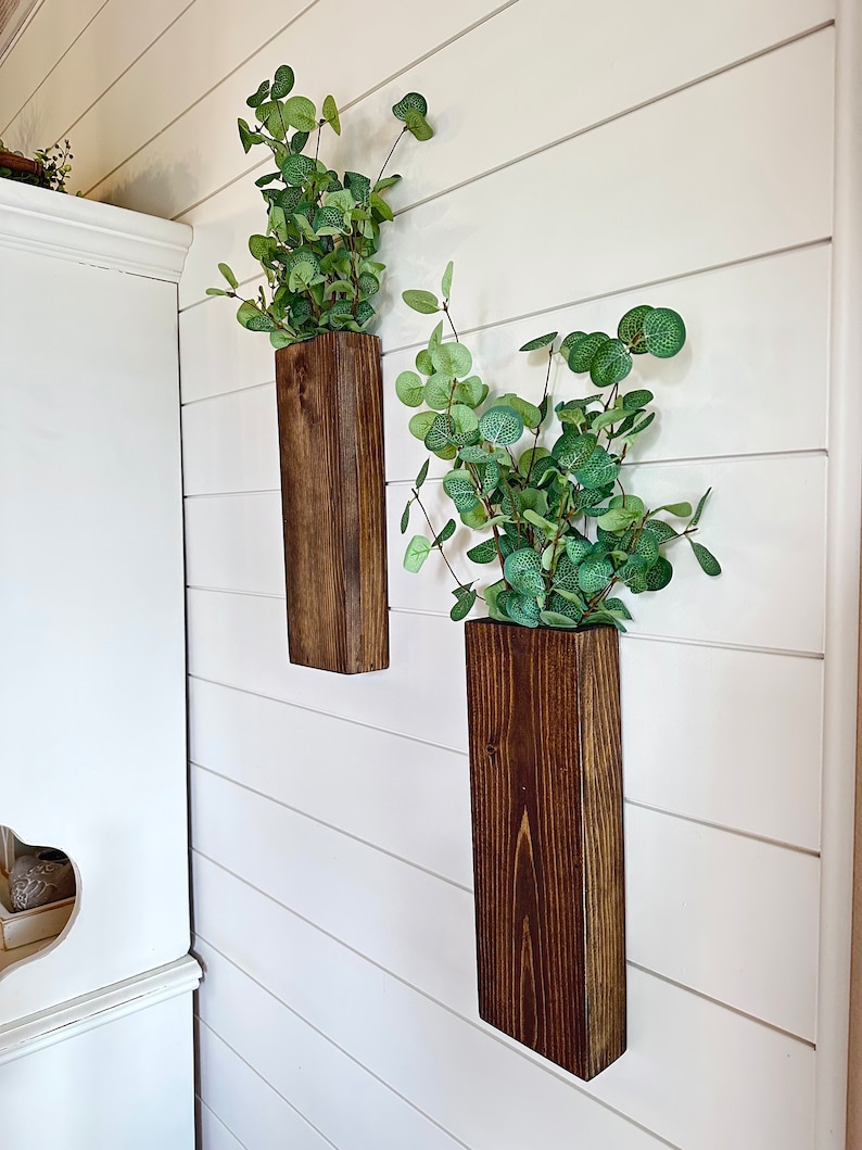 Two handmade rustic wooden wall sconces with a dark, rich wood finish. Wood color is customizable. Each planter holds a vibrant faux eucalyptus plant. Minimalist yet elegant design making this piece perfect for a rustic, farmhouse or bohemian style