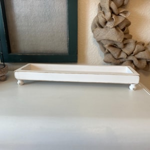 May include: White rectangular tray with a distressed finish and four small feet. The tray is made of wood and has a rustic farmhouse style.