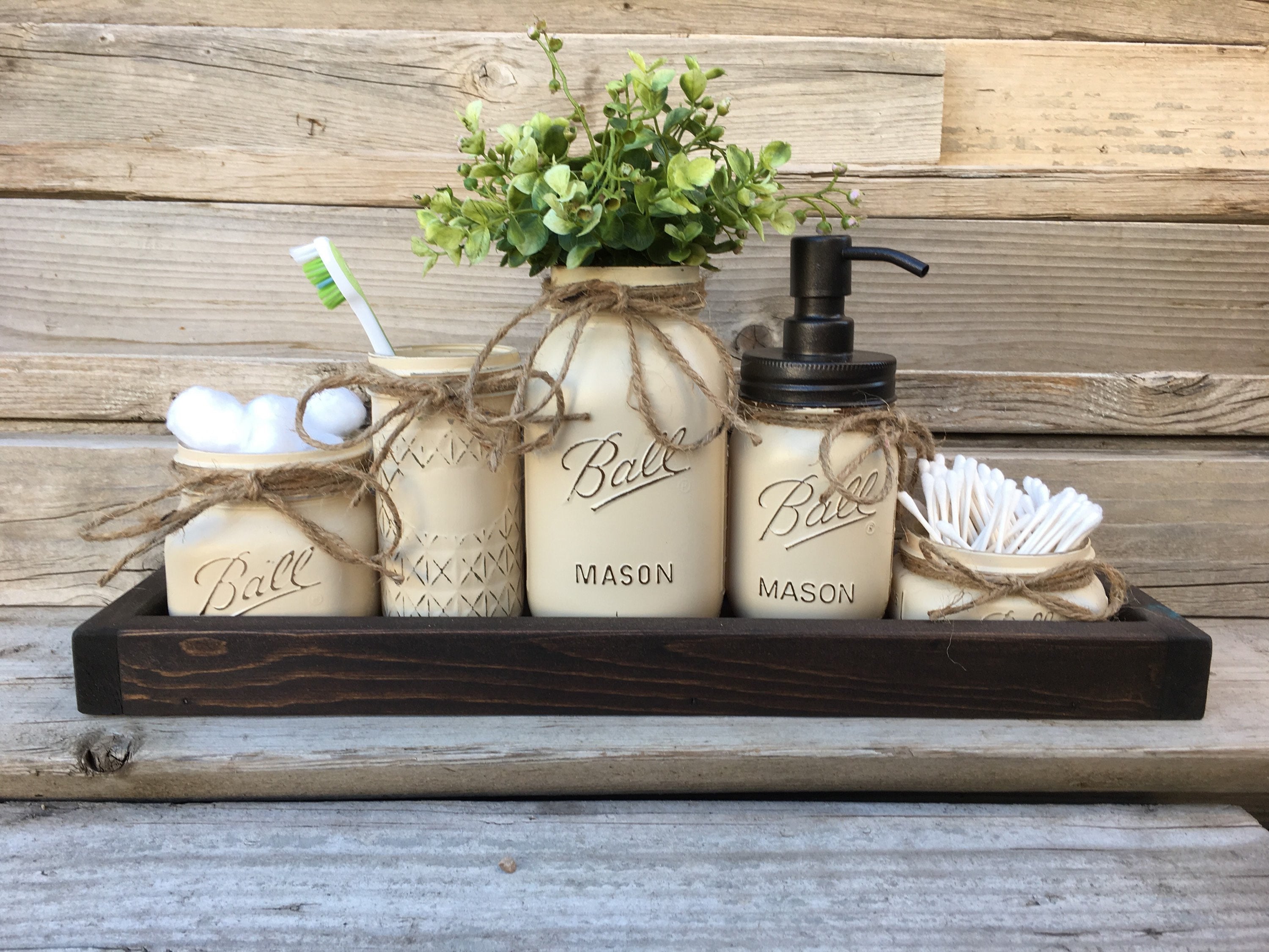 Juego de baño con decoración rústica de granja, tarros de cristal pintados, dispensador de jabón de bronce frotado con aceite, tarros de almacenamiento, hisopos y portacepillos de dientes.