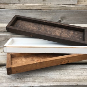 May include: Three wooden trays stacked on top of each other. The top tray is dark brown, the middle tray is white, and the bottom tray is a lighter brown.