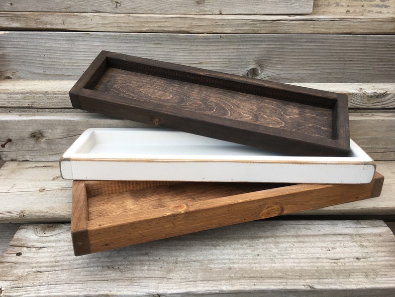 May include: Three wooden trays stacked on top of each other. The top tray is dark brown, the middle tray is white, and the bottom tray is a lighter brown.
