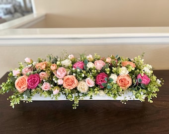 May include: A white rectangular planter filled with a floral arrangement of pink, peach, and white roses, greenery, and small white flowers.