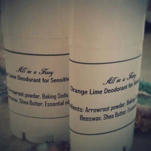 May include: Two white deodorant sticks with black labels. The label on the left stick reads "All in a Fizzy Lime Deodorant for Sensitive Skin" and lists ingredients: "Arrowroot powder, Baking Soda, Beeswax, Shea Butter, Essential oil". The label on the right stick reads "All in a Fizzy Orange Lime Deodorant for Sensitive Skin" and lists ingredients: "Arrowroot powder, Baking Soda, Beeswax, Shea Butter, Essential oil".