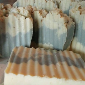 May include: A close-up of several handmade bars of soap. The soap is white with a gray swirl design. The soap is in a rippled pattern.