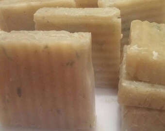 May include: A stack of rectangular bars of handmade soap with a light brown color and a subtle green fleck throughout.