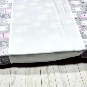 May include: A white fitted sheet with a gray and pink pattern of bears. The sheet is tucked into a mattress and the edge of the sheet is visible.