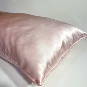Könnte beinhalten: Ein weiches, hellrosa Satin-Kissenbezug. Der Kissenbezug ist glatt und faltenfrei, mit einem dezenten Glanz.