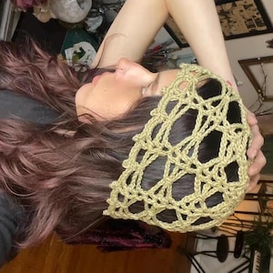 Peut inclure: Un bandeau en crochet vert olive clair. Le bandeau est fait d'un motif tissé à mailles ajourées. Le bandeau est porté sur la tête.