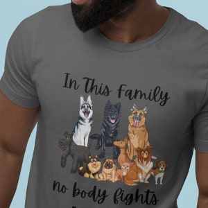 Op de afbeelding: Donkergrijs t-shirt met een afbeelding van verschillende hondenrassen. De tekst "In This Family no body fights ALONE!" staat op het t-shirt. De honden zijn in cartoonstijl afgebeeld.