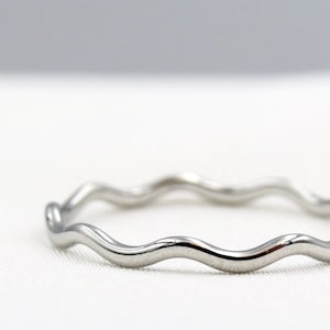 May include: A silver wavy ring. The ring is made of a smooth, shiny metal and has a simple, elegant design.