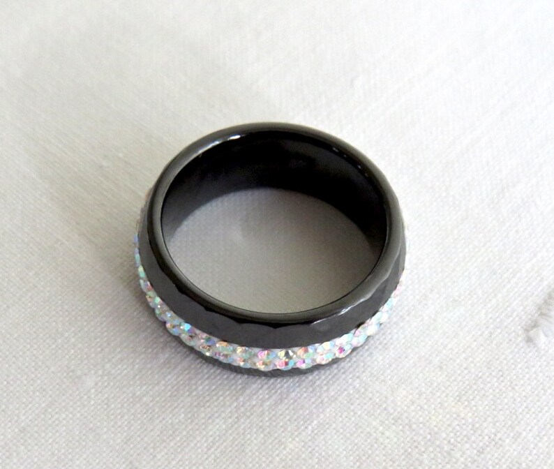 Puede incluir: Un anillo negro con una banda de piedras de imitaci&oacute;n iridiscentes.