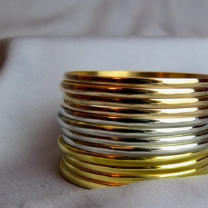 May include: A stack of gold and silver bangles. The bangles are smooth and shiny, reflecting light. The gold bangles are a bright, warm color, while the silver bangles have a cool, metallic sheen. The bangles are stacked on top of each other.