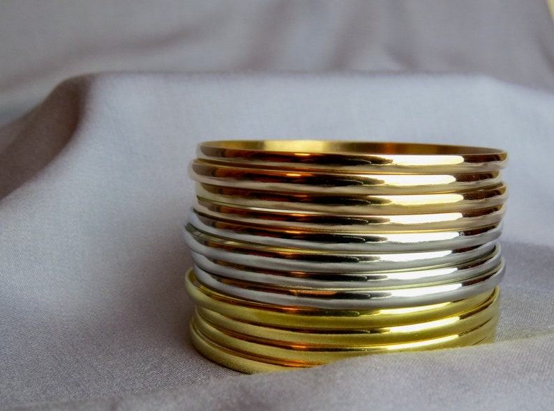 May include: A stack of gold and silver bangles. The bangles are smooth and shiny, reflecting light. The gold bangles are a bright, warm color, while the silver bangles have a cool, metallic sheen. The bangles are stacked on top of each other.