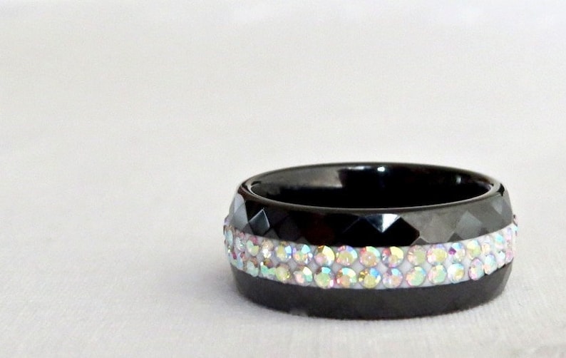 Puede incluir: Un anillo negro con una banda de piedras de imitaci&oacute;n iridiscentes.