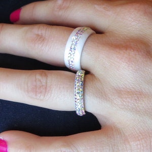 Puede incluir: Dos anillos de silicona blancos con filas de piedras de cristal iridiscentes. Los anillos se llevan en el &iacute;ndice y el dedo medio de una mano.