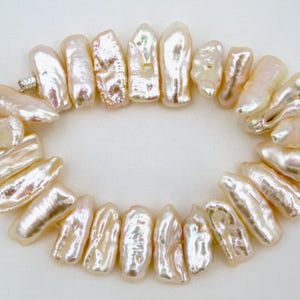 May include: A necklace composed of irregularly shaped, lustrous, off-white pearls. The pearls are strung together, forming a circular shape. The pearls have a natural, organic appearance, with variations in color and texture.