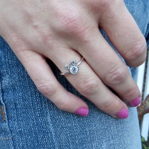 May include: A silver ring with three small clear stones set in a Mickey Mouse shape.