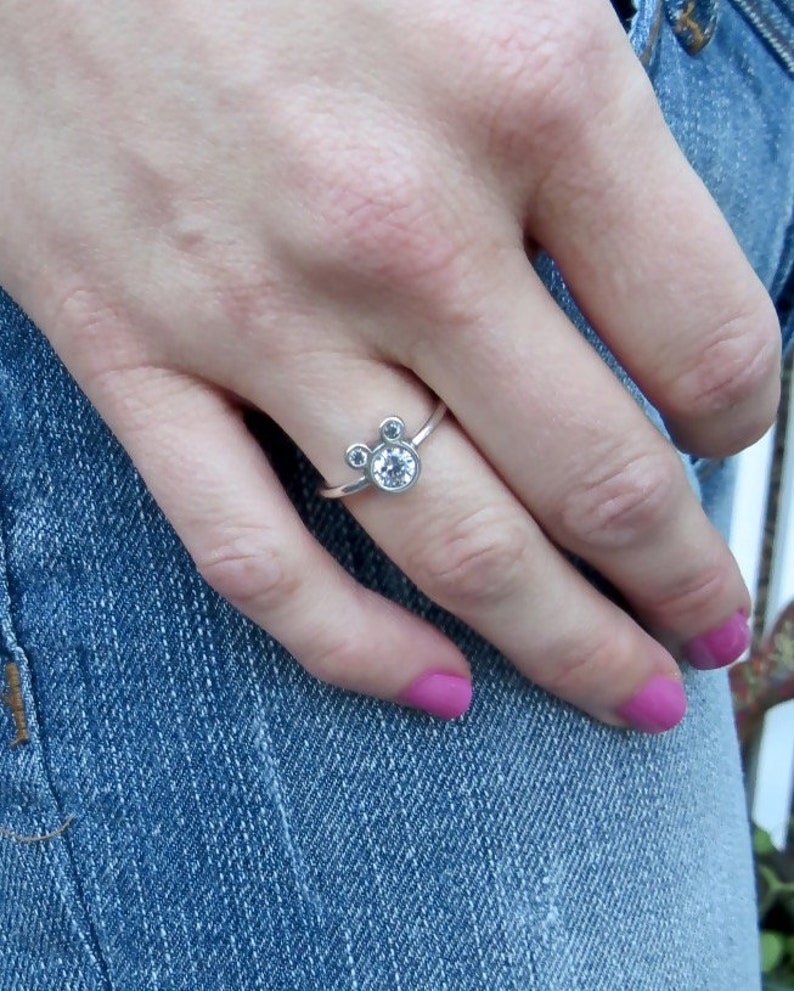 May include: A silver ring with three small clear stones set in a Mickey Mouse shape.