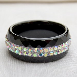 Puede incluir: Un anillo negro con un borde biselado y dos filas de piedras de imitaci&oacute;n iridiscentes.