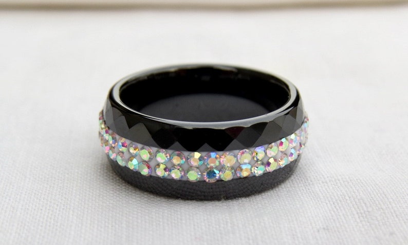Puede incluir: Un anillo negro con un borde biselado y dos filas de piedras de imitaci&oacute;n iridiscentes.