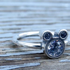 May include: A silver ring with a clear crystal Mickey Mouse head design.