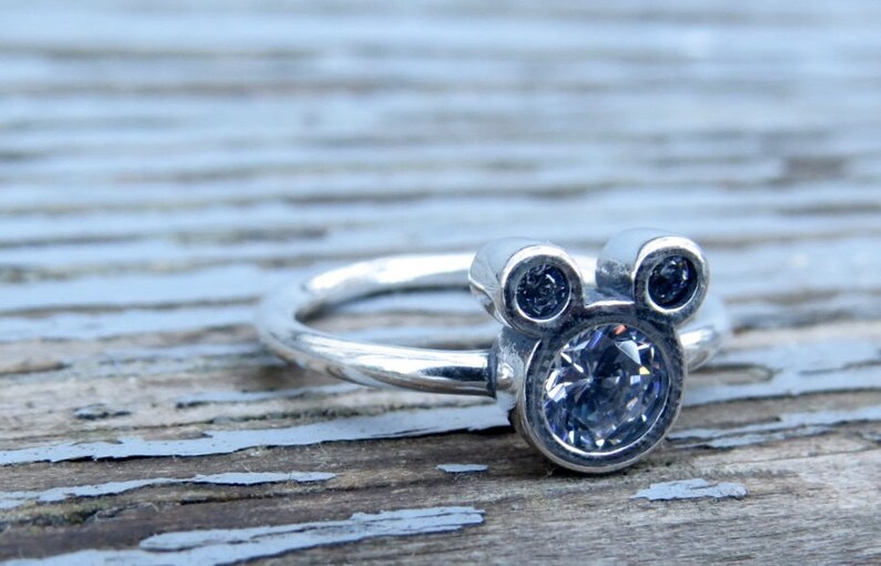 May include: A silver ring with a clear crystal Mickey Mouse head design.