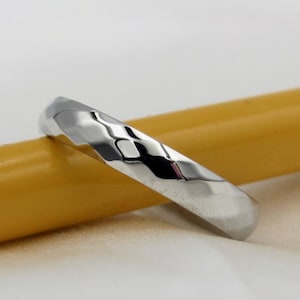 Puede incluir: Una banda plateada con textura martillada. La banda está sobre una superficie amarilla.