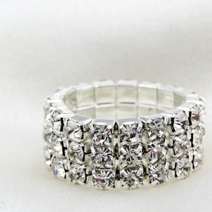 May include: A silver ring with three rows of clear rhinestones. The ring is stretchy and adjustable.
