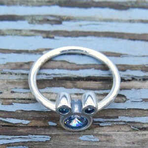 May include: A silver ring with a clear iridescent stone in the center, shaped like Mickey Mouse's head.