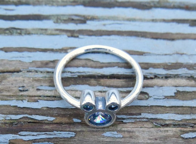 May include: A silver ring with a clear iridescent stone in the center, shaped like Mickey Mouse's head.