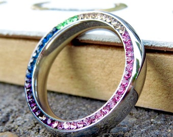 Puede incluir: Un anillo de plata con un arcoíris de piedras preciosas de colores engastadas alrededor de la banda.