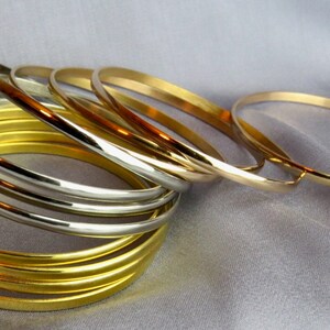 May include: A collection of gold and silver bangles. The bangles are stacked and arranged on a light gray, silky surface. The gold bangles have a bright, shiny finish, while the silver bangles have a polished, metallic appearance. The jewelry is simple and elegant.