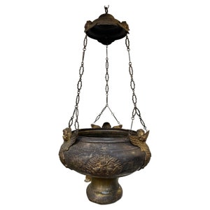 May include: A vintage, ornate, hanging censer with a dark bronze finish and gold accents. The censer has a round, open top and is suspended from a chain. It features decorative cherub figures and a detailed design.