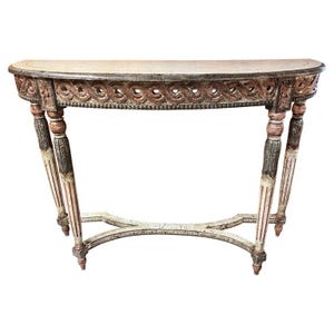 May include: A semi-circular console table featuring a weathered finish with muted tones of gray, white, and faded red. The apron displays a carved repeating wave pattern, supported by four slender, fluted legs connected by a curved X-stretcher.