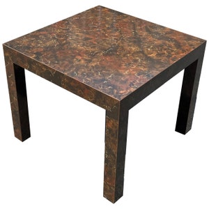 May include: A square, brown coffee table with a marbled top and black legs. The table has a unique, rustic look.