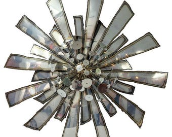 May include: A unique, starburst-shaped chandelier with a metallic finish. The fixture features numerous rectangular and circular metal elements radiating from a central point. The edges of the metal pieces have a darker, contrasting border, adding depth to the design.
