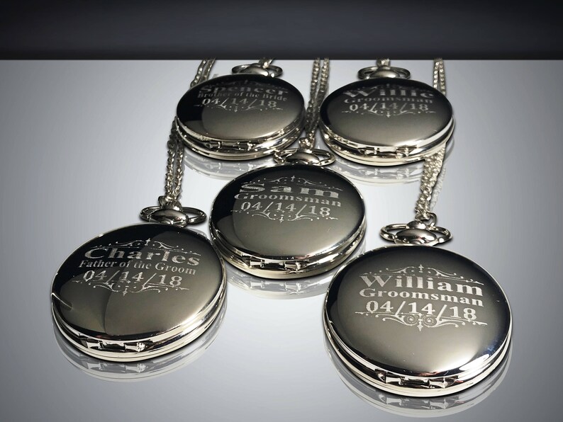 May include: Five silver pocket watches with chains, each engraved with a name and the date 04/14/18. The names are Charles, Father of the Groom, Spencer, Sam Groomsman, Willie Groomsman, and William Groomsman.