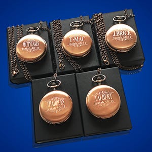 May include: Five antique-style pocket watches with chains, each engraved with a name and the scripture Isaiah 40:31. The watches are displayed on black velvet boxes.