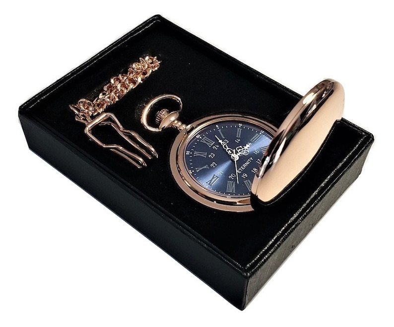 K&ouml;nnte beinhalten: Eine ros&eacute;goldene Taschenuhr mit blauem Zifferblatt und r&ouml;mischen Ziffern f&uuml;r die Stunden. Die Uhr befindet sich in einer schwarzen Samtbox mit einer Kette.