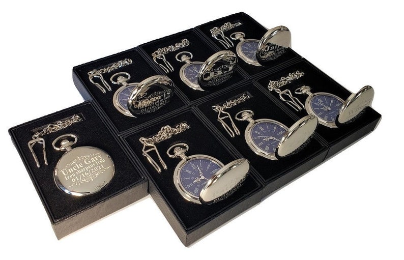 K&ouml;nnte beinhalten: Acht silberne Taschenuhren mit blauen Zifferbl&auml;ttern werden in schwarzen Samtboxen pr&auml;sentiert. Jede Uhr wird mit einer Kette und einem Anh&auml;nger geliefert. Eine Uhr tr&auml;gt die Inschrift "Uncle Gary from Sharpes from 01/10/2021".