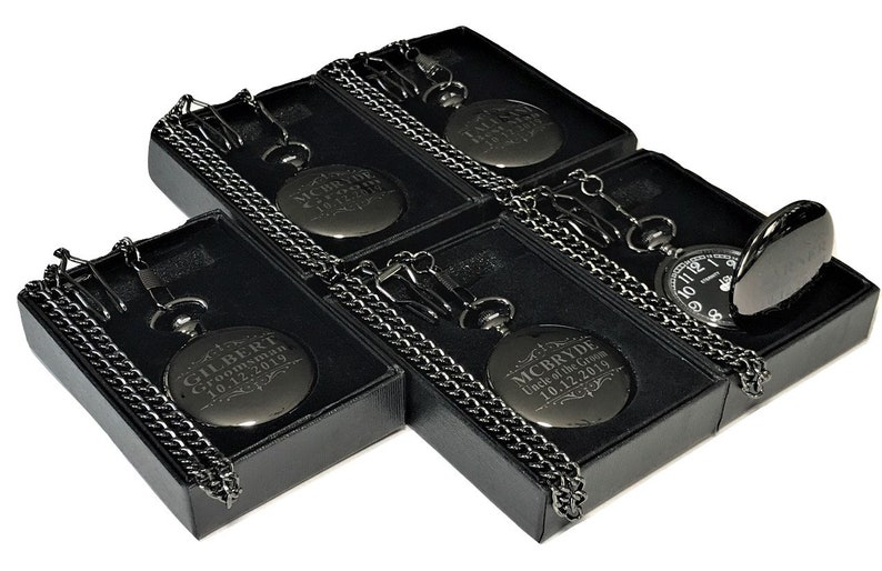 K&ouml;nnte beinhalten: F&uuml;nf schwarze Taschenuhren mit Ketten in schwarzen Samtboxen. Jede Uhr hat eine andere Inschrift auf der Vorderseite. Die Inschriften beinhalten Namen und Daten.