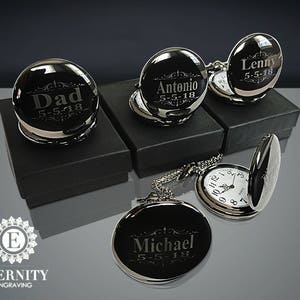 May include: Four silver pocket watches with engraved names and dates. The watches are on black boxes and a white surface. The watches have a chain attached to them.