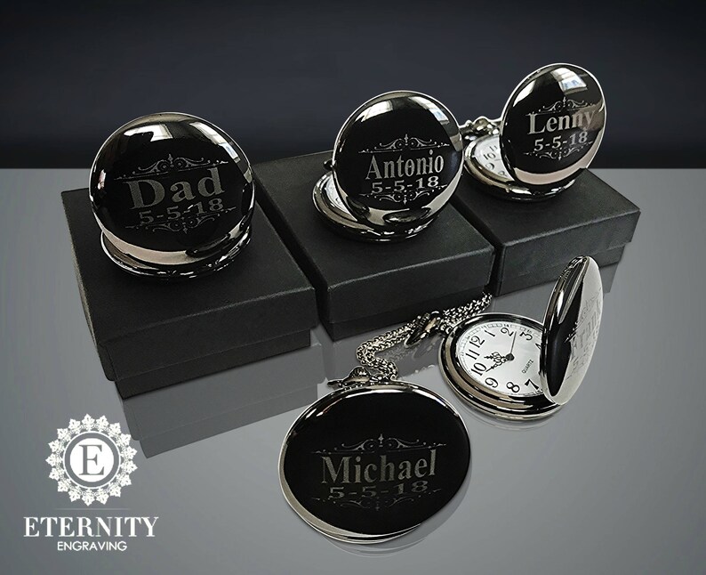 May include: Four silver pocket watches with engraved names and dates. The watches are on black boxes and a white surface. The watches have a chain attached to them.
