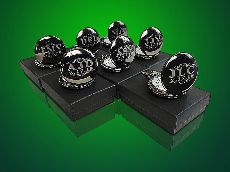 May include: A collection of eight silver pocket watches with engraved initials and dates. The watches are arranged on black boxes with a green background.